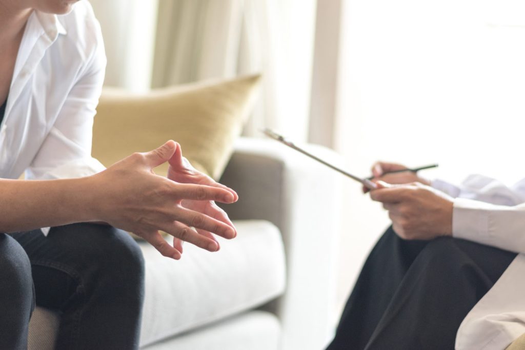 Foto de terapeuta com uma prancheta de anotações e paciente sentado em sessão de psicoterapia individual